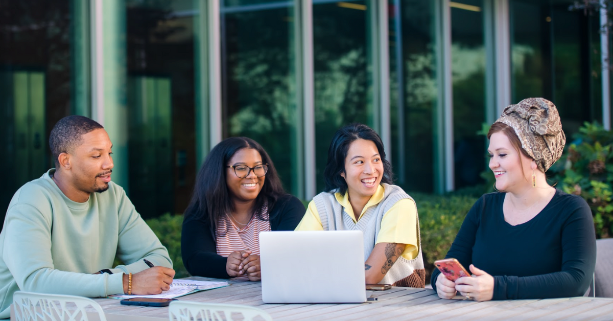 A group of four Capital One associates sit around a laptop outside at a table