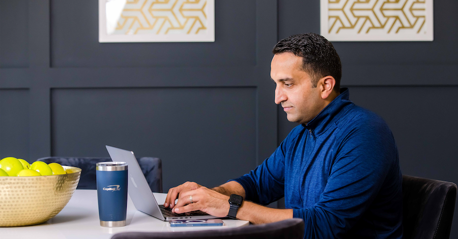 Ahmed, Capital One associate, sits at his laptop and works, in front of a dark blue/gray wall