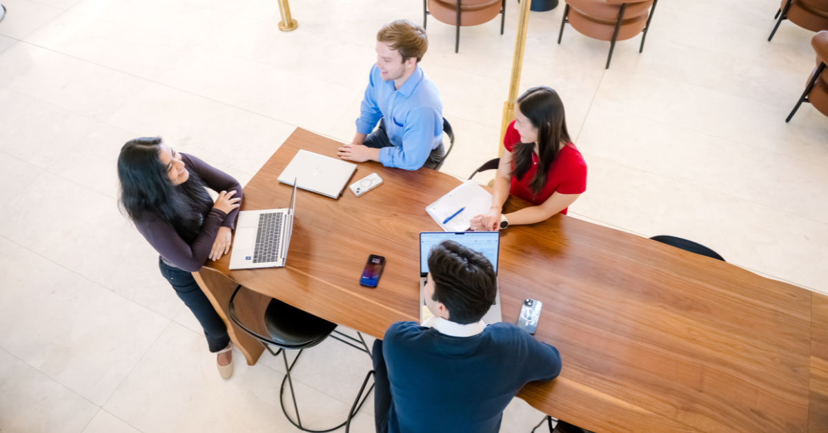 Four Capital One associates sit around a table with their laptops and talk