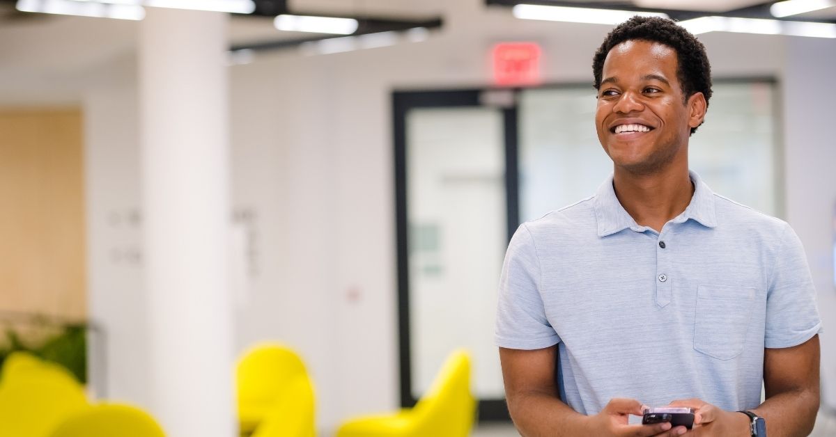 Capital One associate wears a light blue polo shirt and holds a phone in his hands, smiling