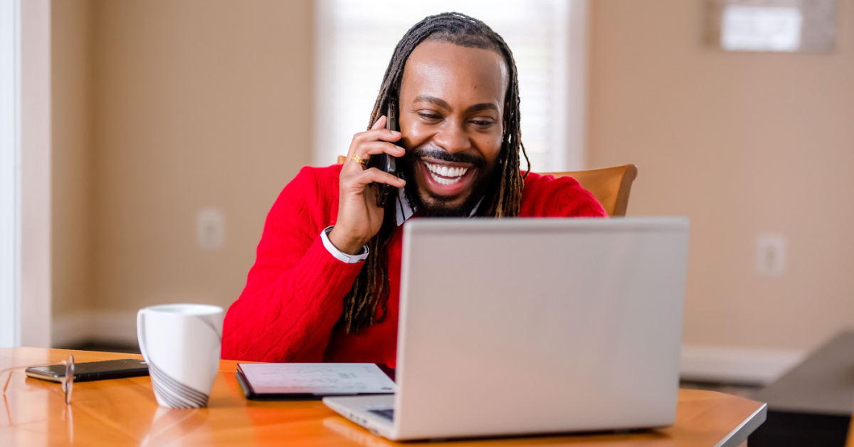 Capital One Customer Care associate talks on the phone while looking at his laptop, wearing a red sweater