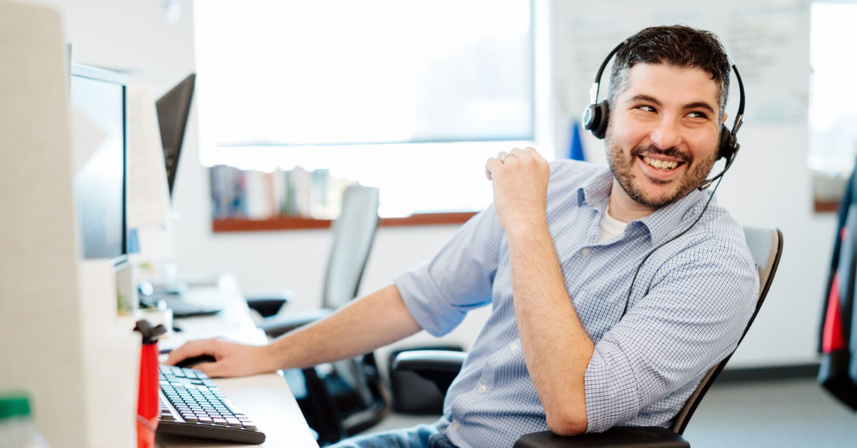 Capital One Customer Care associate works at his desk, leaning back in his chair smiling wearing a headset