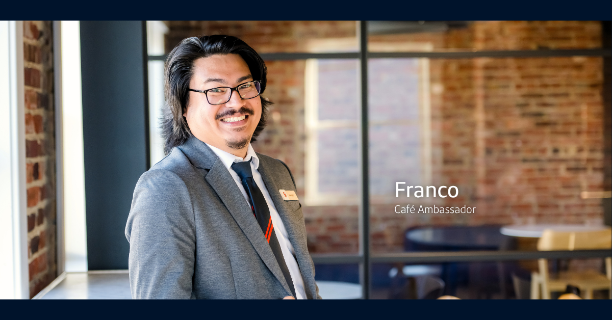 Capital One Café ambassador Franco wears a gray suit jacket and smiles over his right shoulder at the camera