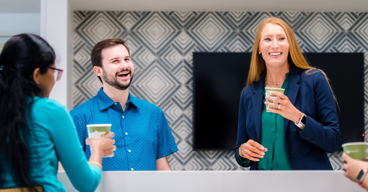 Capital One associates stand around a break table with cups of coffee talking and laughing