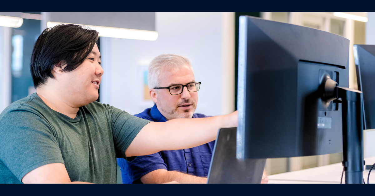 Two Capital One software engineers work together at a desk, pointing at a monitor