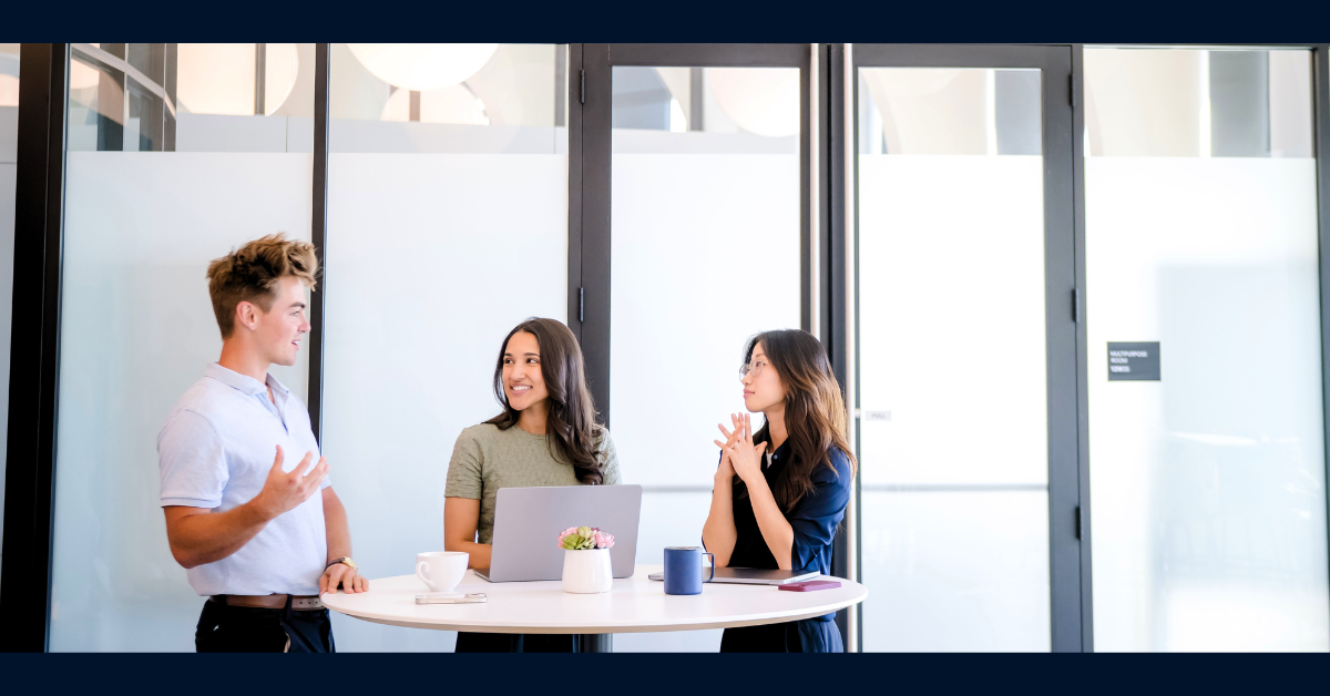 Three Capital One software engineers stand around a white table and talk while laughing and working