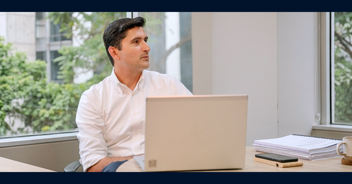 Capital One associate Oz sits at a desk with his laptop and notebook open and is looking away to his left