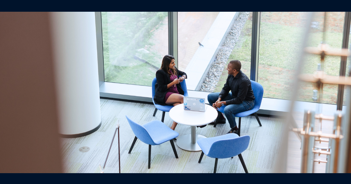 Two Capital One associates sitting in blue chairs by a large window and talking