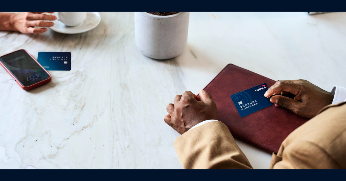 Two Capital One customers sitting at a desk with their Venture X Business credit cards