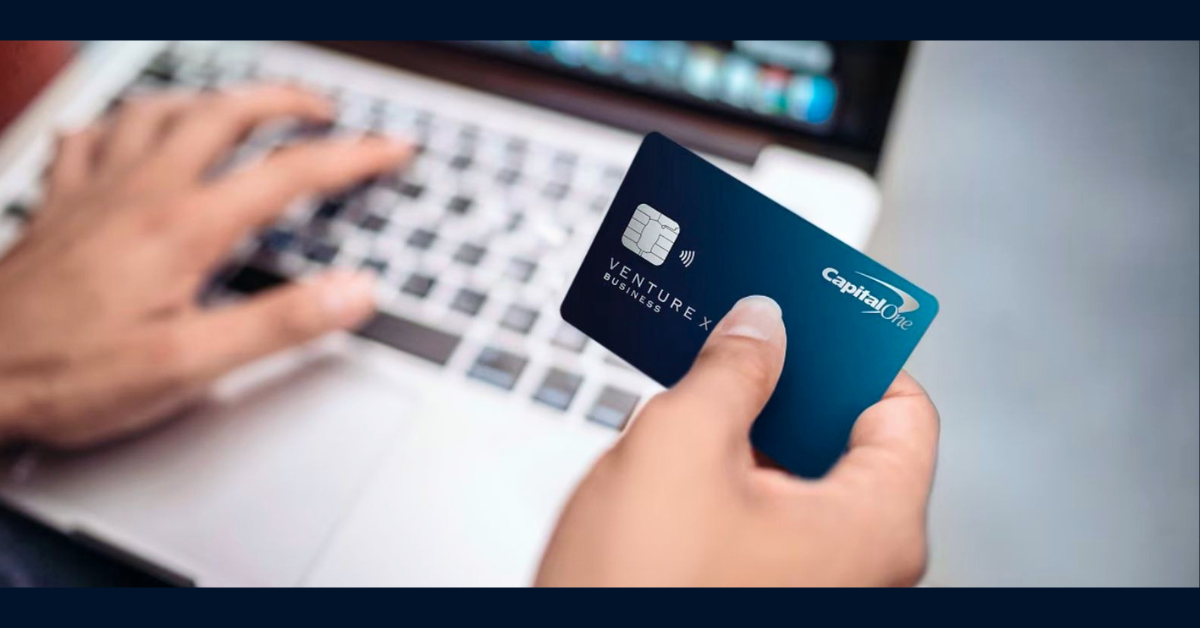 Customer holding a Venture X credit card while typing on their laptop