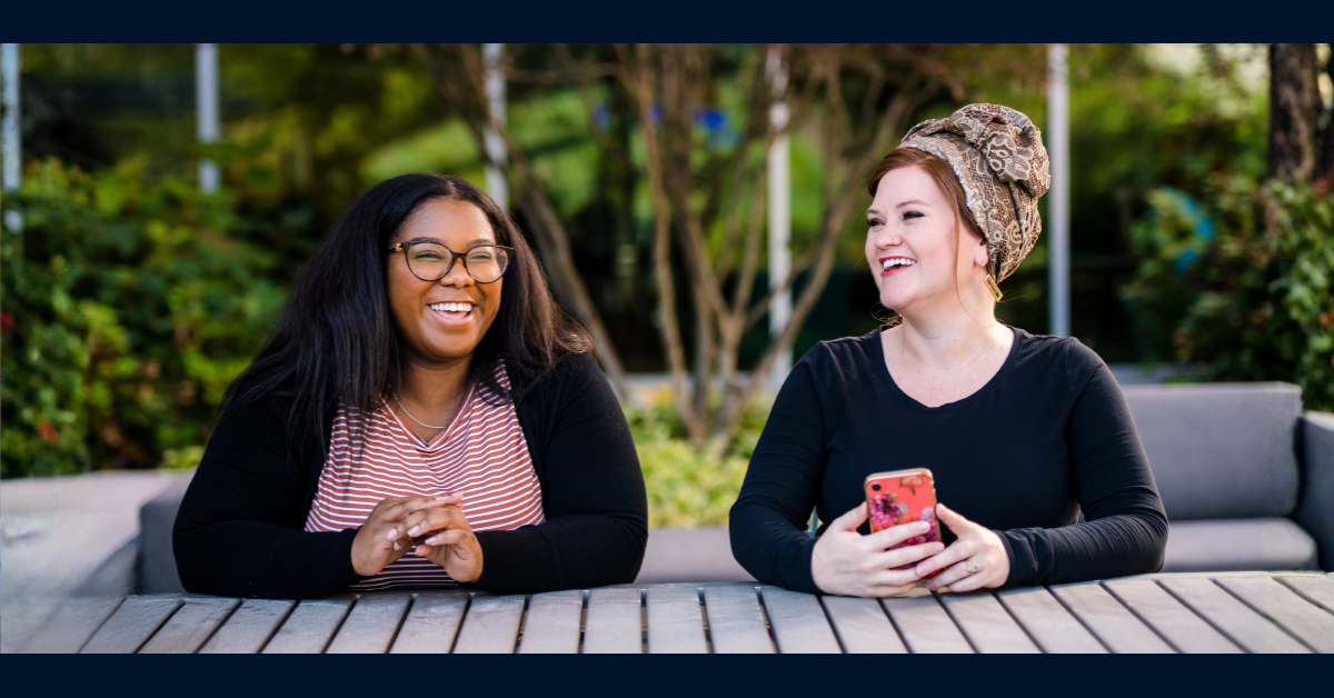 Two Capital One associates sit side by side outdoors, talking and laughing together