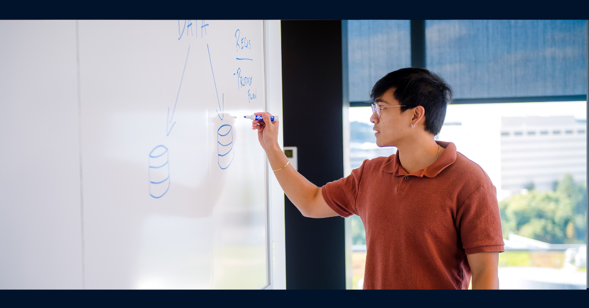 Capital One associate wearing a red polo and glasses draws a diagram on a whiteboard