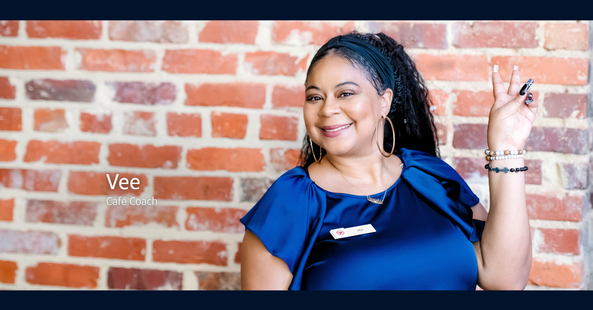 Capital One Café ambassador Vee smiling against a brick wall and holding up a peace sign