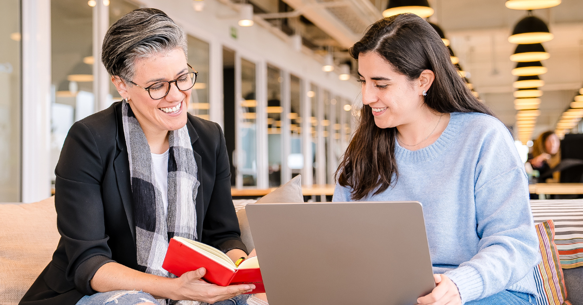 Two Capital One associates smiling over a book and laptop