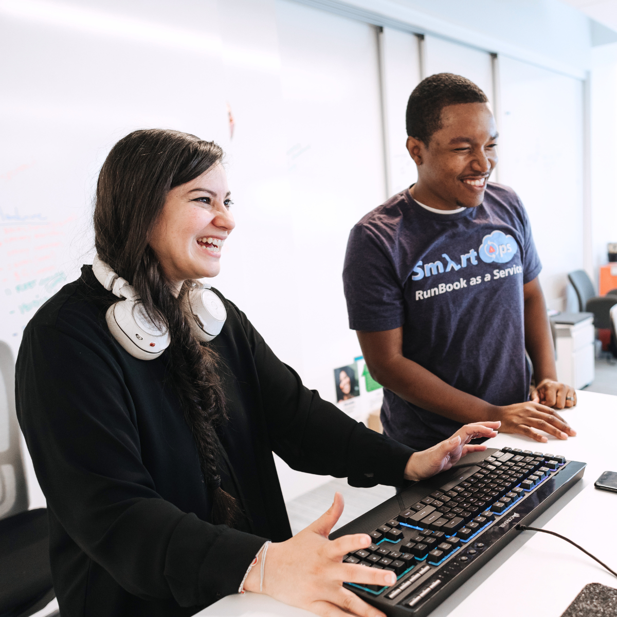 Two associates standing at a desk and laughing while looking at a monitor