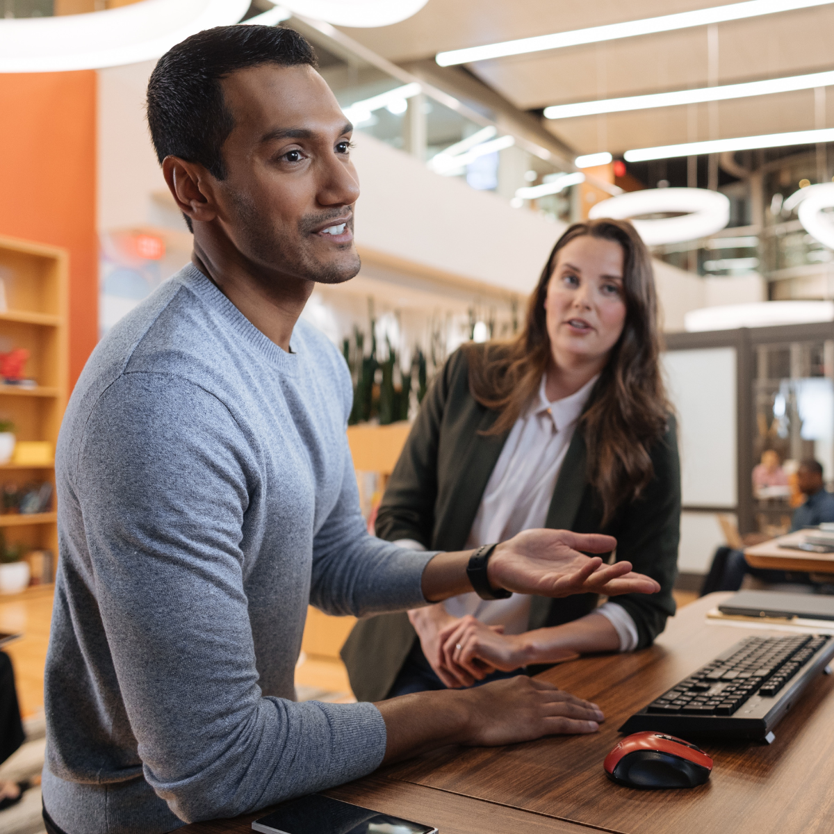 Two associates leaning on a standing desk and talking, with one gesturing to a monitor