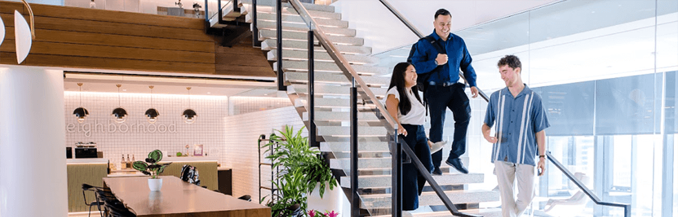 Three employees walking down steps together in an office while conversing.