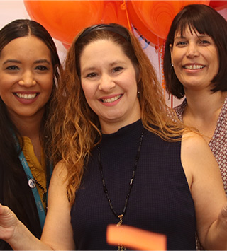 A trio of women employees at a business event, with joyful balloons