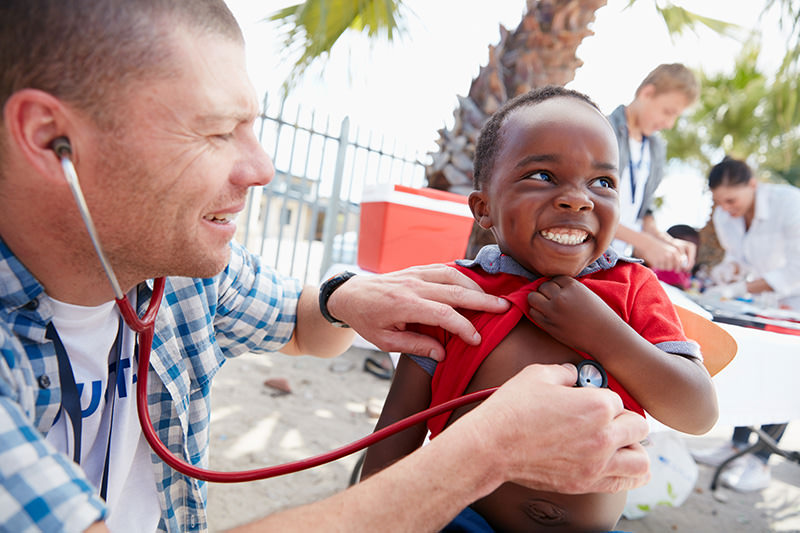 Dr. with stethoscope checking heartbeat of young boy