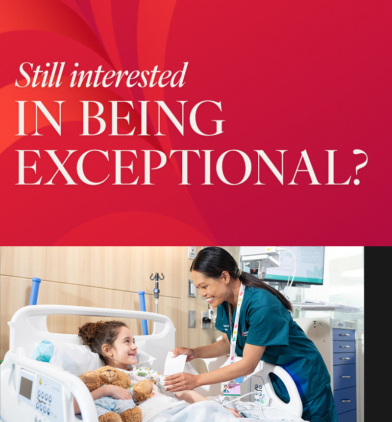 A smiling nurse interacts with a young girl holding a teddy bear lying in a hospital bed.