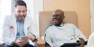 A doctor showing a patient something on a smartphone, both smiling.