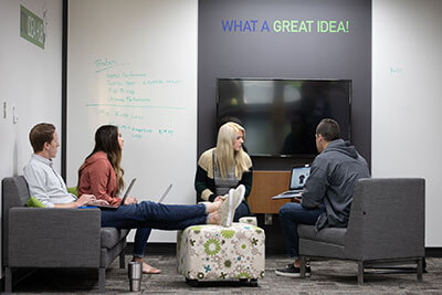 four people sitting in chairs looking at a laptop