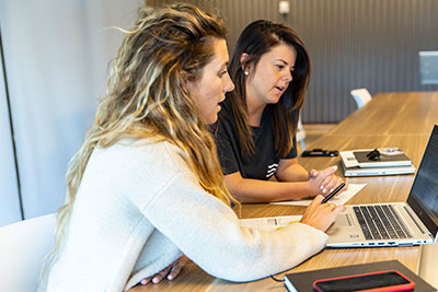 two women sitting at a table looking at a computer