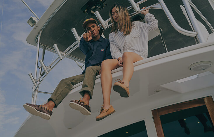Two people sitting on the roof of a boat, pointing at the camera