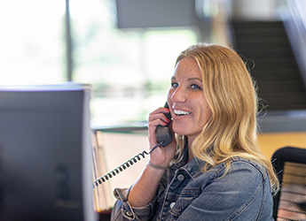 A woman smiles at her desk while talking on a landline phone