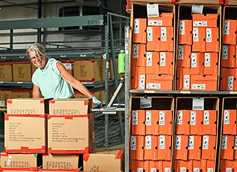 A woman pulls many stacks of shoeboxes on a large cart