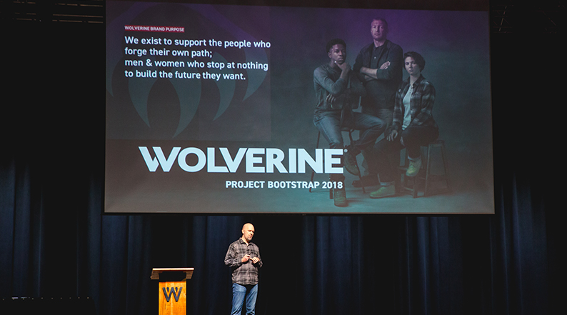 A man stands on a stage with a presentation projected behind him