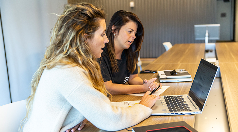 Two women discuss something on a laptop