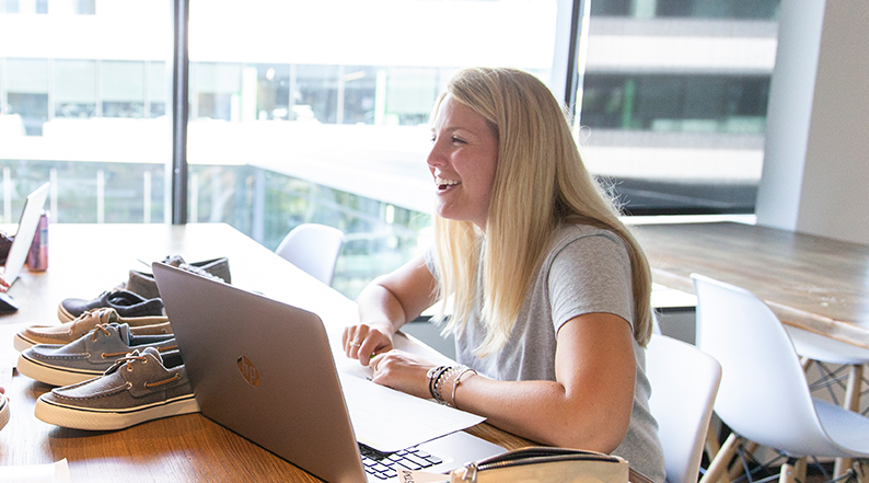 A young woman laughs at her computer, surrounded by shoe samples