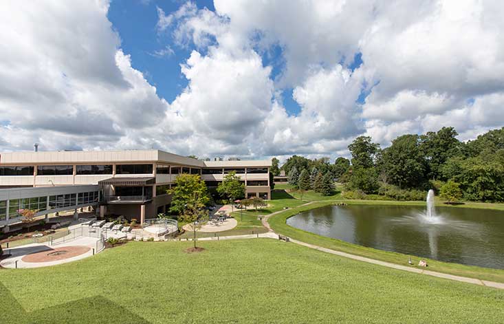 A concrete building next to greenery and a body of water