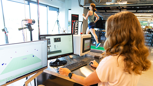 A woman sits at a computer monitor while Darby runs on the same treadmill