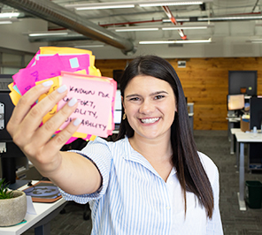 A woman smiles at the camera holding a stack of Post-it Notes