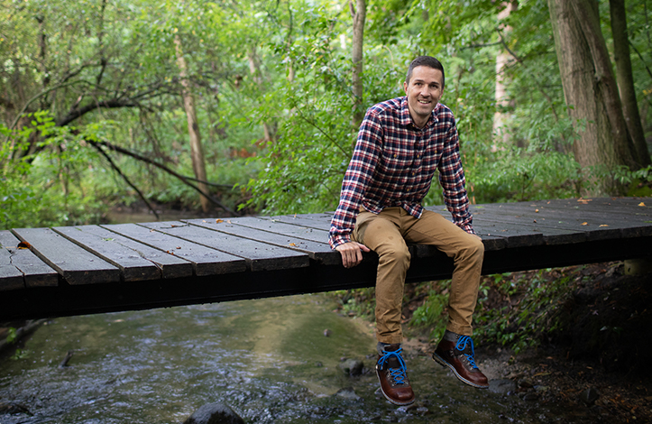 A man sits on a bridge in a wooded area