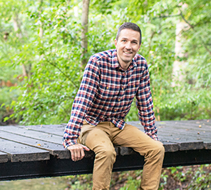 A man sits on a bridge in a wooded area