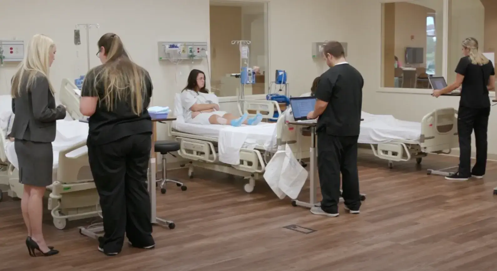 Play Video: Photo of a hospital treatment room with student doctors observing patients.