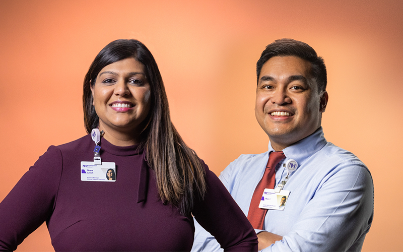 A woman and man smile while posing in front of a tan background. They are wearing business attire and Northwestern Medicine badges. 