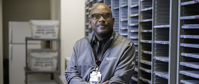 Portrait of Lionel Cooper in Mail Services, wearing glasses and a gray jacket with Northwestern Medicine logo.