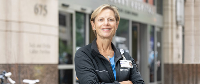 Portrait of Cheryl Dann, BSN, RN, CPAN posing with arms crossed in front of a hospital building.