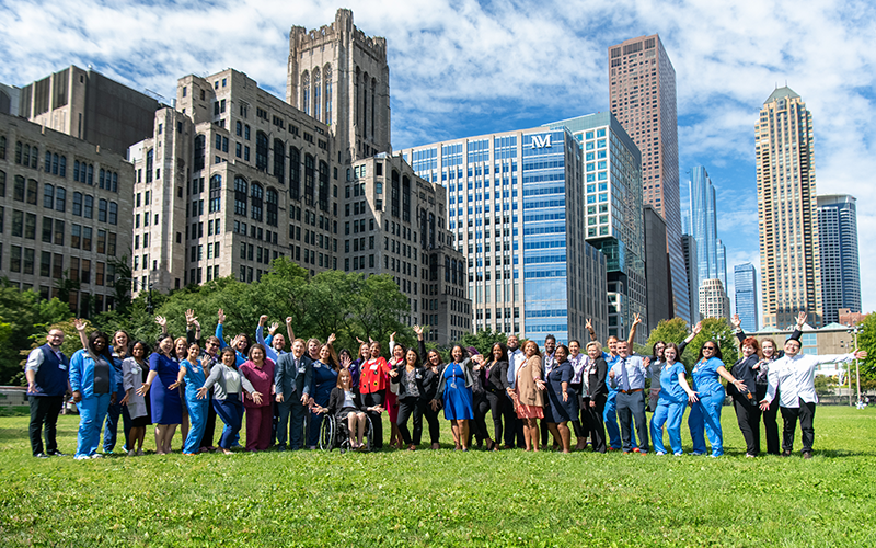 Members of the NM Champion Network pose on a lawn in front of several Northwestern Medicine buildings. Other buildings of the Chicago skyline can be seen in the background. 