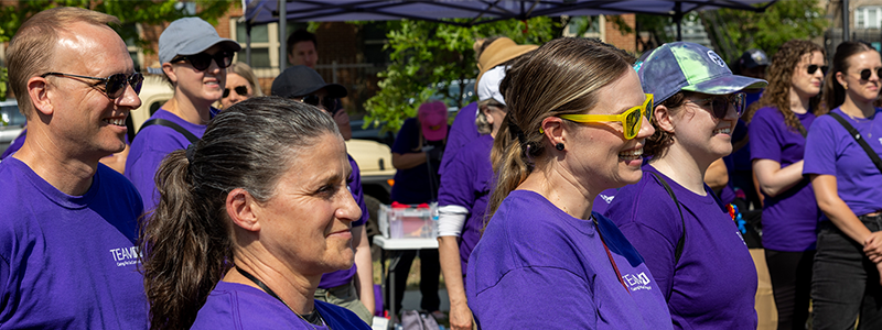 Several Northwestern Medicine employees in purple shirts stand outside during a volunteer event on a sunny day. 
