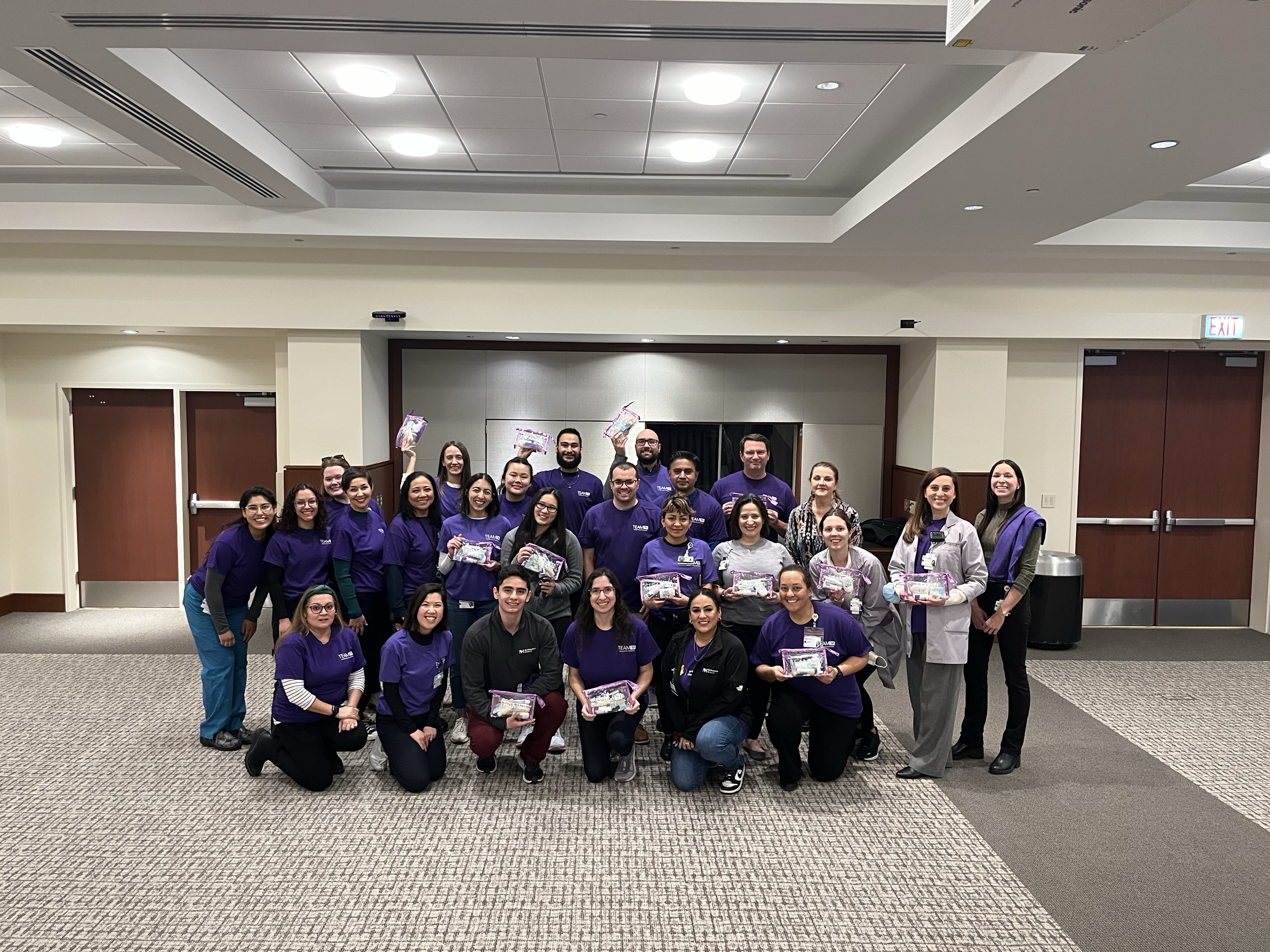 A group of people wearing purple shirts poses for a photo with small bags filled with hygiene items.