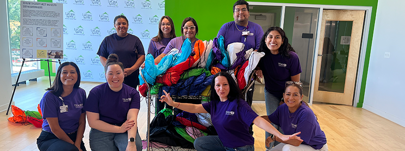 A group of people wearing purple shirts poses for a photo with small bags filled with hygiene items.