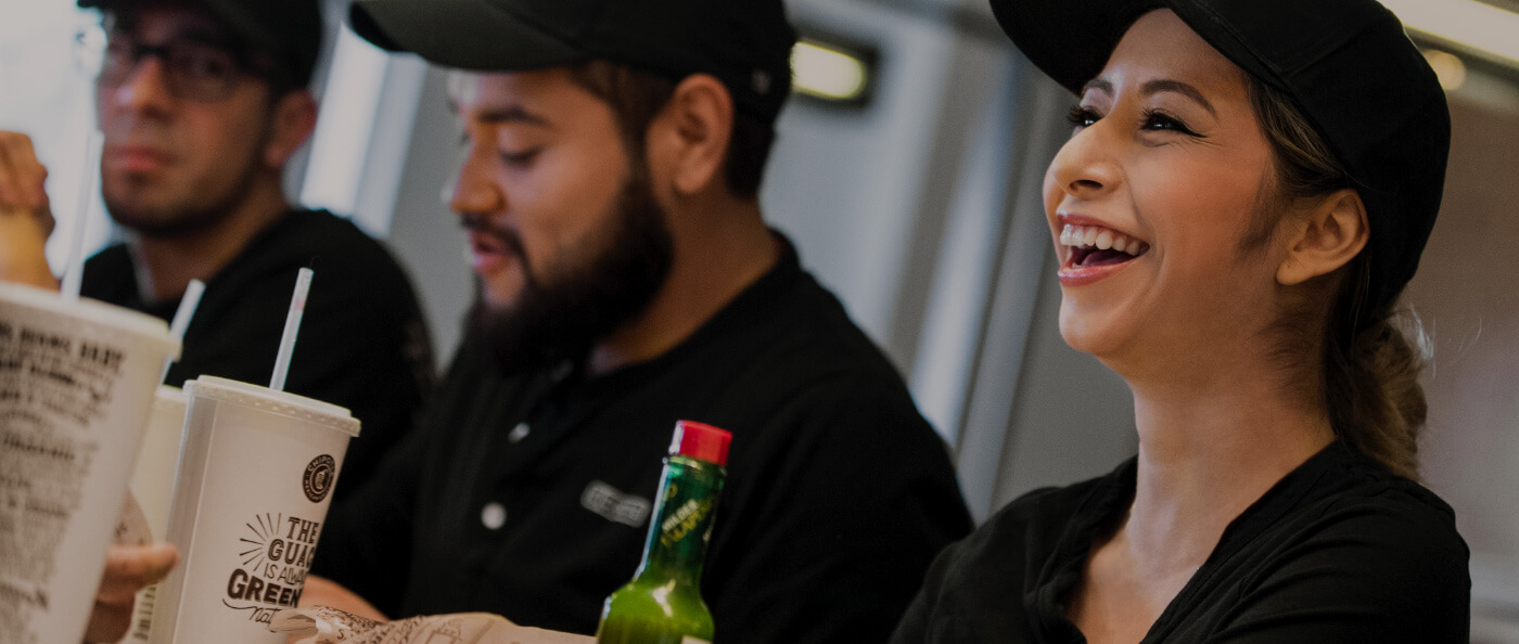 Chipotle Restaurant Crew team members laugh and enjoy a family-style meal together in the restaurant.