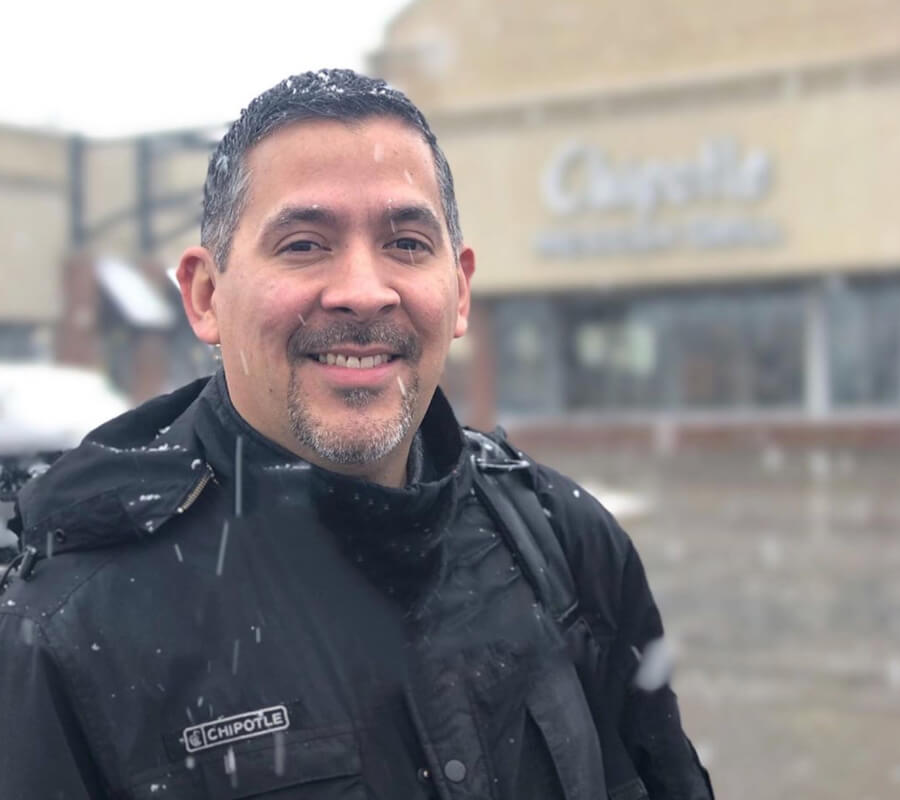 Chipotle leader German happily stands outside of a Chipotle restaurant in the cold weather to share his leadership journey.