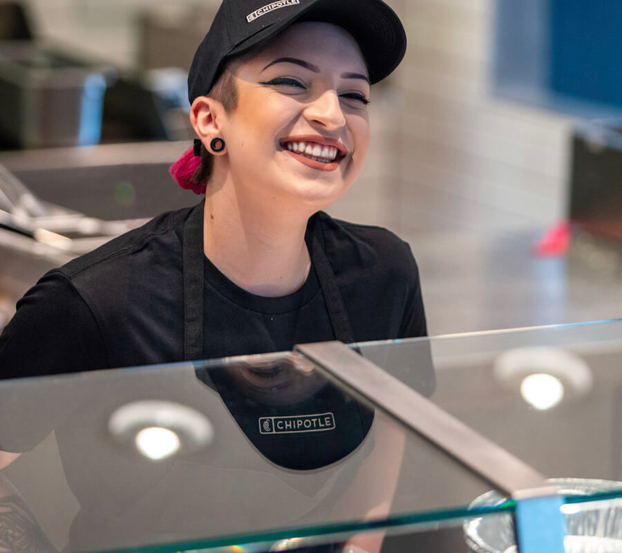 Crew member happily serves Chipotle bowls and burritos to restaurant guests.