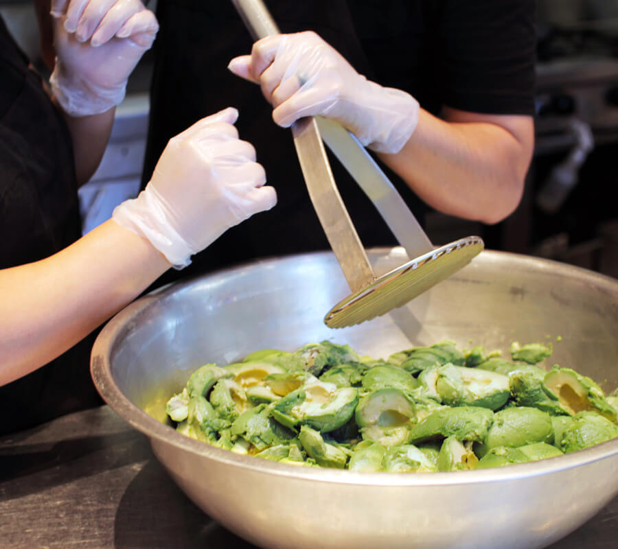 Chipotle Crew members make handmashed guac daily with large avocado masher in a stainless steel bowl.